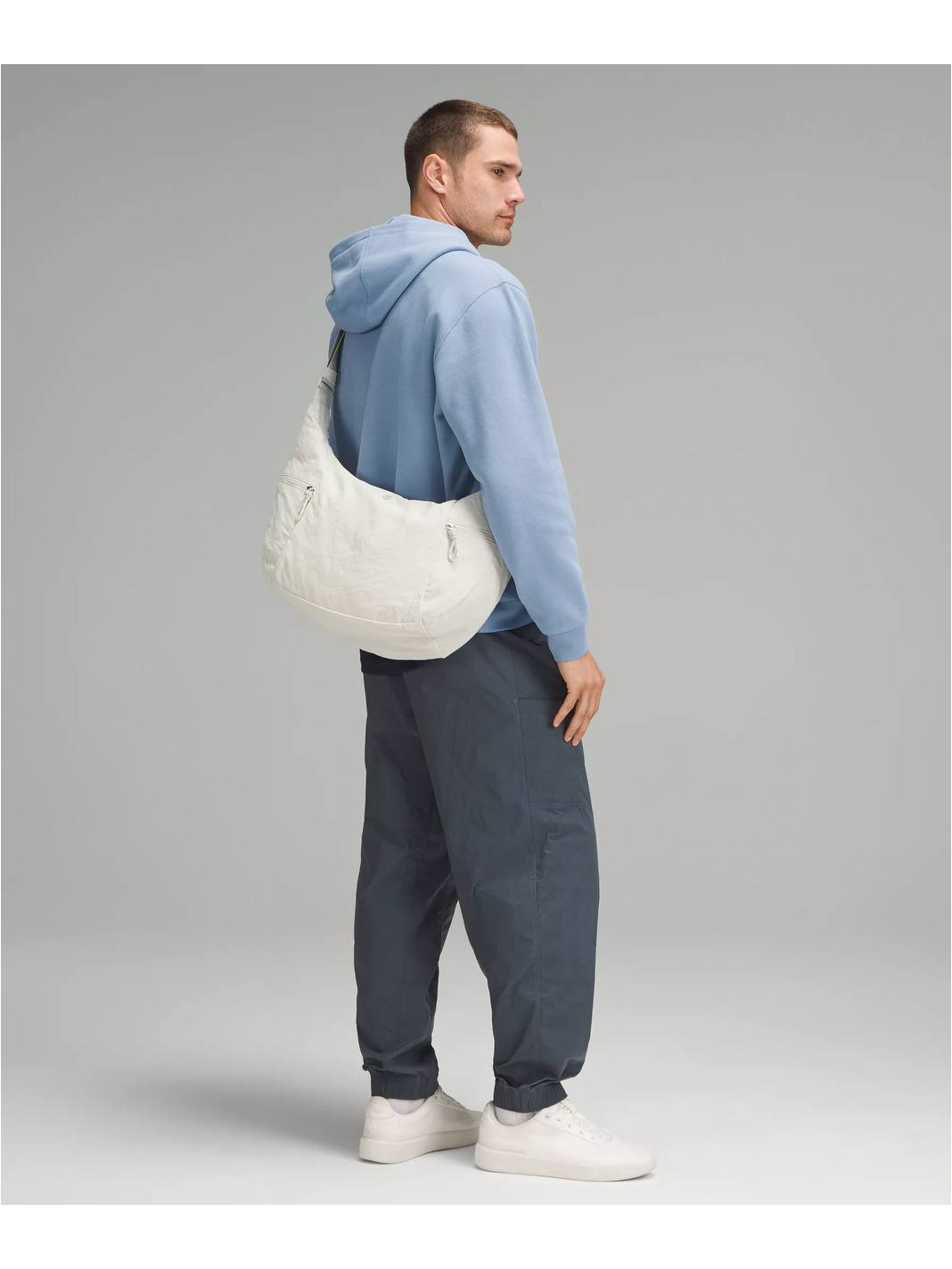 کیف اسلوچی اسلینگ 13 لیتری Lululemon، کیف اسلینگ کرم روی پشت مدل با هودی آبی روشن و شلوار تیره