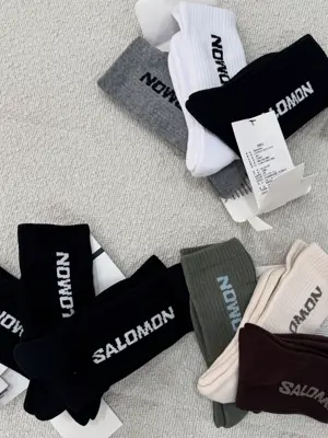 پک‌های جوراب ساق بلند Salomon مشکی و ترکیب‌های سفید و طوسی، کرم و زیتونی و قهوه‌ای روی زمینه روشن
