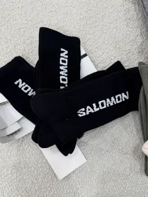 پک سه‌جفتی جوراب ساق بلند مشکی Salomon با نوشته سفید و بافت کبریتی روی زمینه روشن