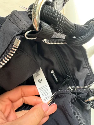 کیف کانورتیبل Lululemon مشکی؛ نمای نزدیک آستر، برچسب داخلی، زیپ و حلقه اتصال بند پاراکورد