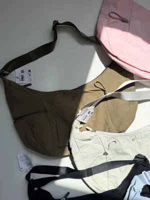 کیف اسلوچی اسلینگ Lululemon 13L؛ نمای نزدیک کیف سبز زیتونی کنار رنگ‌های صورتی و شیری