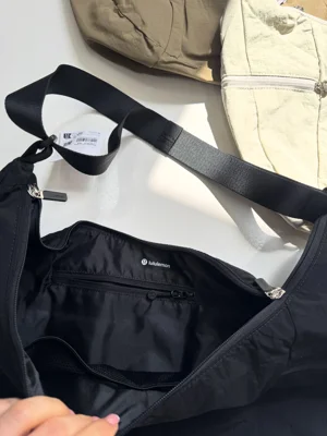 کیف اسلوچی اسلینگ Lululemon 13L مشکی؛ فضای داخلی باز و بند روی زمینه کیف‌های روشن