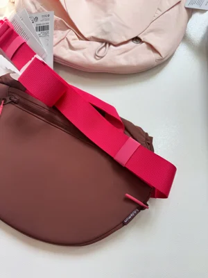 نمای پشت کراس بادی کرو Lululemon قهوه‌ای با بند سرخابی؛ بخشی از کیف صورتی و تگ‌ها در بالا