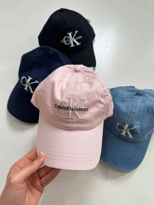 کلاه بال کپ Calvin Klein Jeans صورتی در دست با گلدوزی CK و نقاب خمیده، کنار رنگ‌های مشکی، سورمه‌ای و آبی