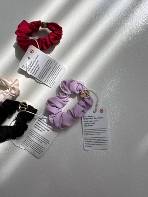 نمای نزدیک کش مو Lululemon قرمز، یاسی و مشکی با پارچه چین‌دار و نشان طلایی روی زمینه روشن