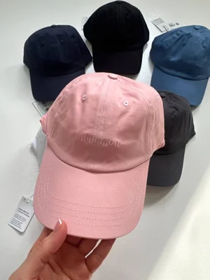 کلاه بال کپ کلاسیک Lululemon صورتی در دست با گلدوزی هم‌رنگ و دوخت‌های نقاب، کنار رنگ‌های دیگر