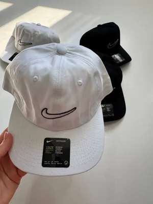 نمای جلوی کلاه بال کپ Nike سفید در دست با Swoosh تیره، نقاب خمیده و سوراخ‌های دوردوزی
