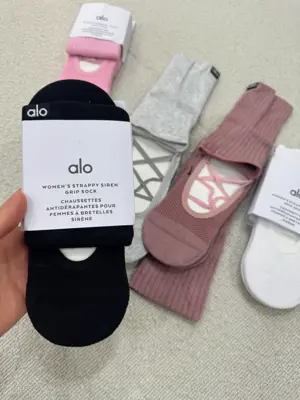 نمای نزدیک بسته‌بندی جوراب پیلاتس ALO مشکی با نوشته Women's Strappy Siren Grip Sock در دست