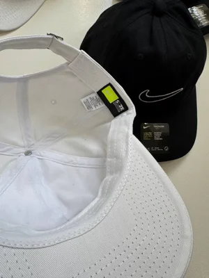 کلاه بال کپ Nike سفید با لبه داخلی بازشده، نوار دور سر و سگک پشت؛ نمونه مشکی کنار آن