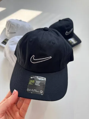 نمای نزدیک کلاه بال کپ Nike تیره در دست با لوگوی خطی روشن و دوخت نقاب - تصویر اصلی
