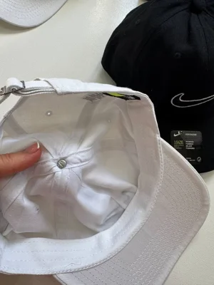 نمای داخل کلاه بال کپ Nike سفید با دوخت‌های تاج و پشت نقاب؛ کلاه مشکی کنار آن