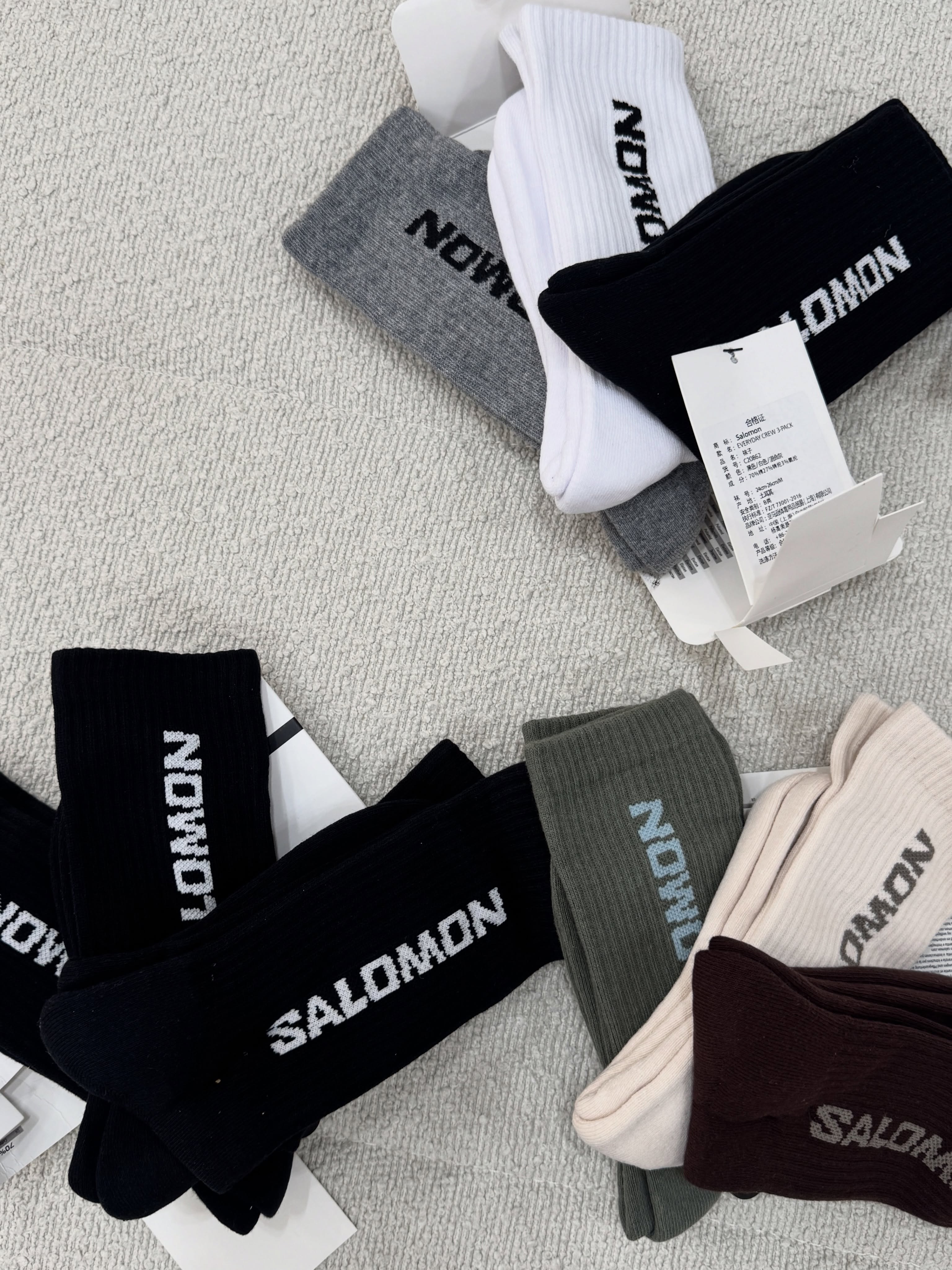 پک‌های جوراب ساق بلند Salomon مشکی و ترکیب‌های سفید و طوسی، کرم و زیتونی و قهوه‌ای روی زمینه روشن
