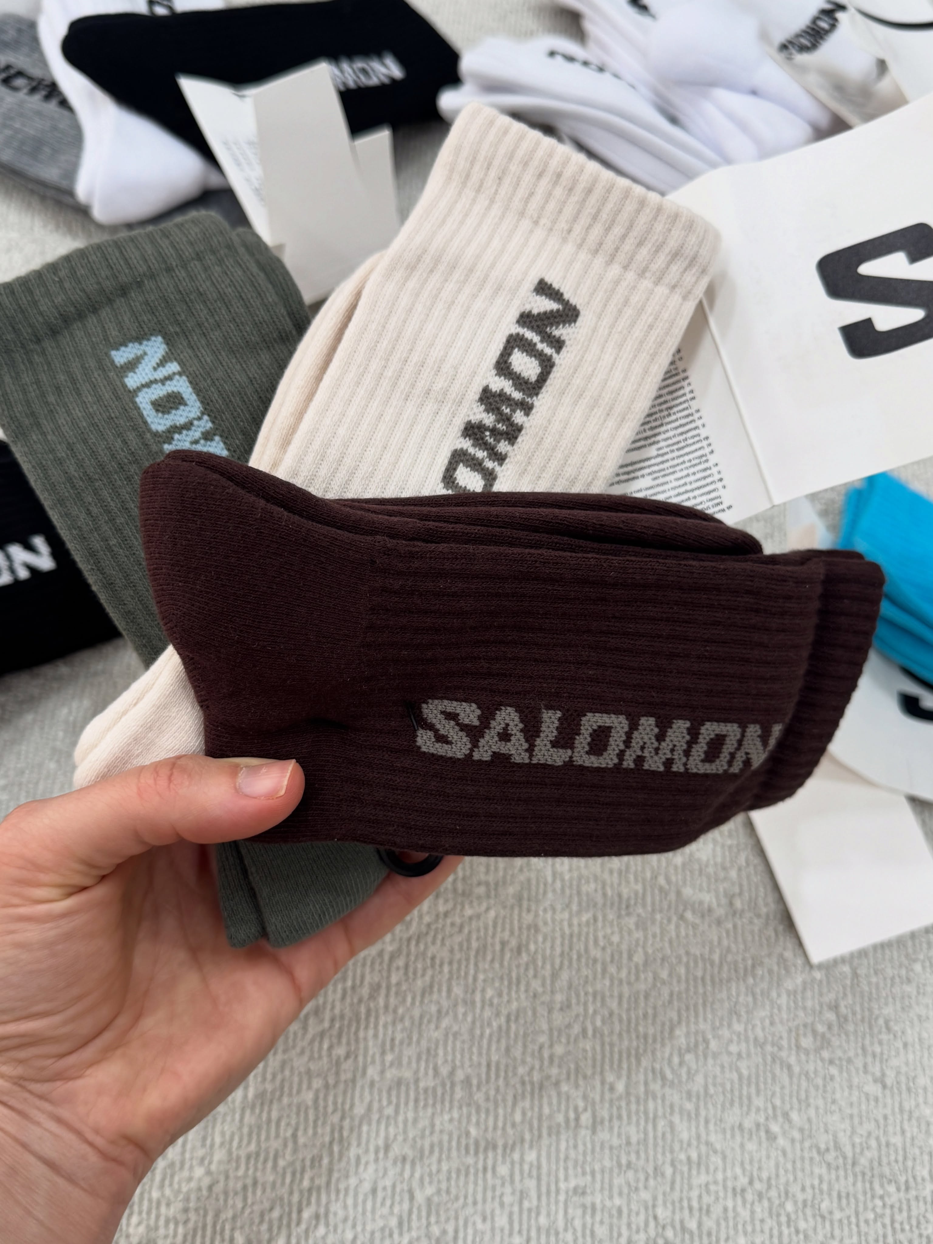 پک سه‌جفتی جوراب ساق بلند Salomon قهوه‌ای، کرم و زیتونی در دست با نوشته روی ساق