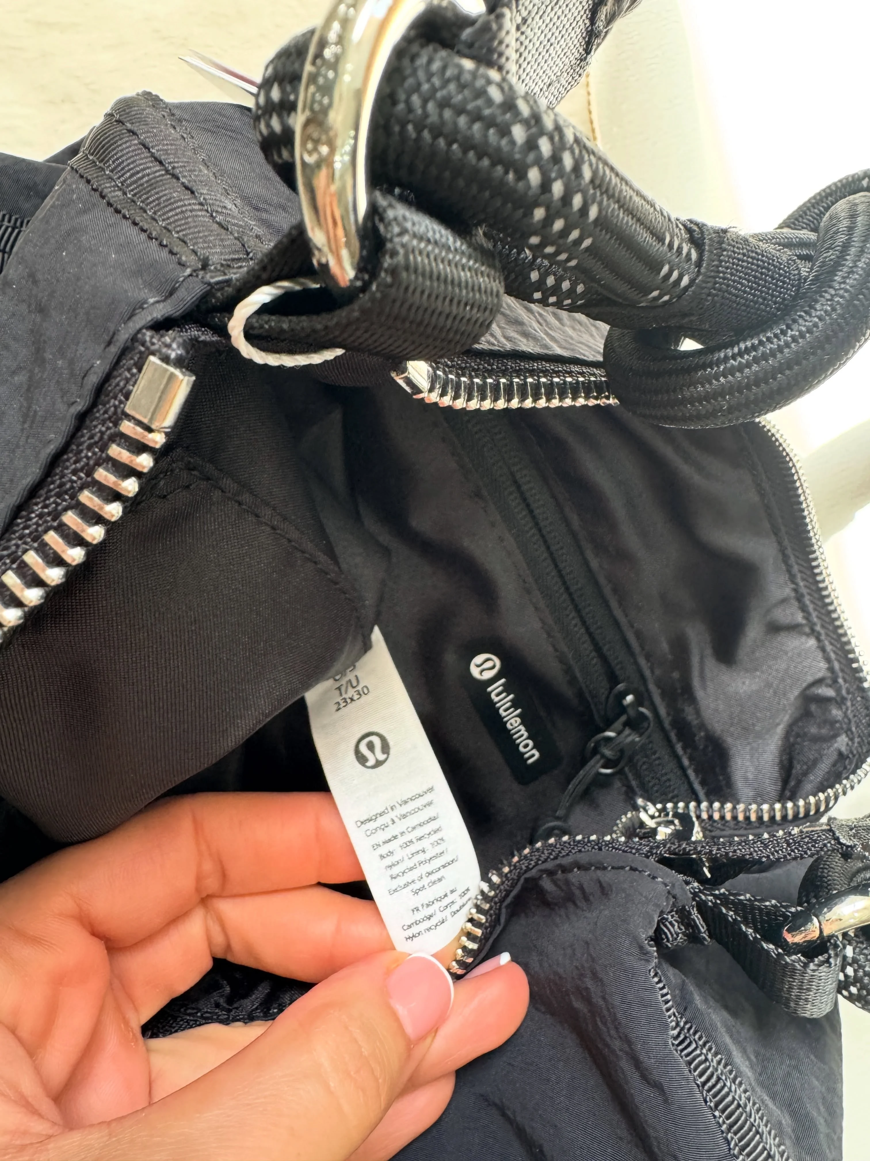 کیف کانورتیبل Lululemon مشکی؛ نمای نزدیک آستر، برچسب داخلی، زیپ و حلقه اتصال بند پاراکورد