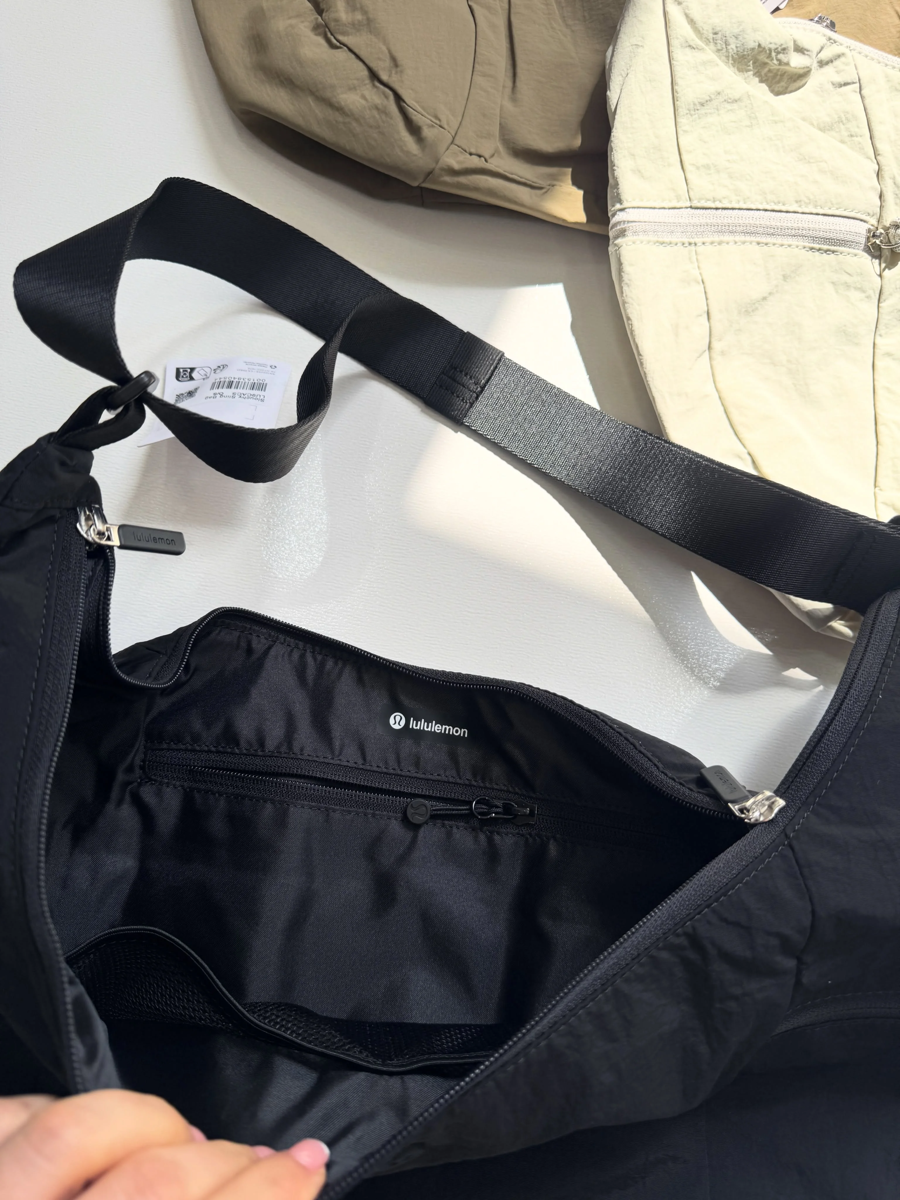 کیف اسلوچی اسلینگ Lululemon 13L مشکی؛ فضای داخلی باز و بند روی زمینه کیف‌های روشن