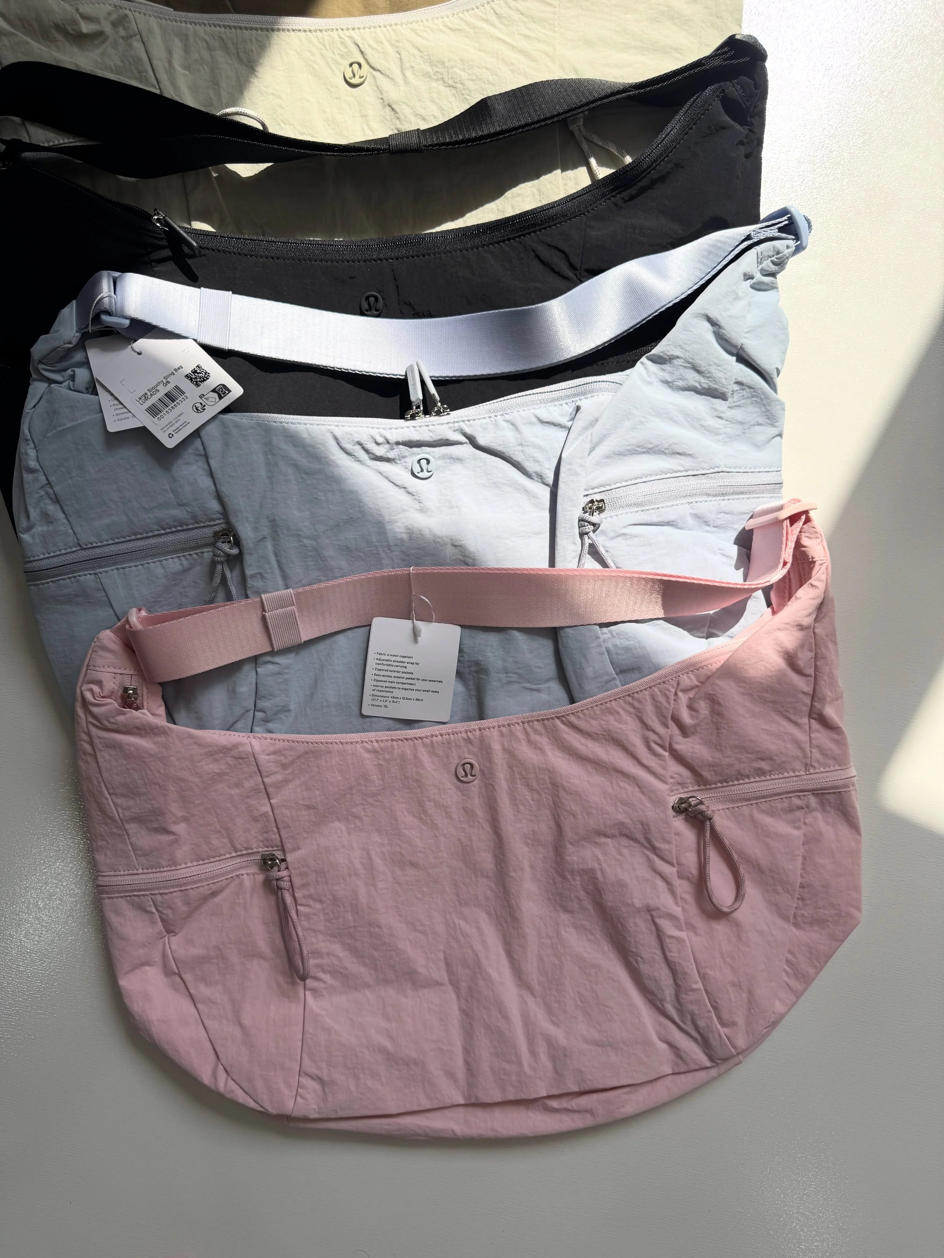 کیف اسلوچی اسلینگ Lululemon 13L؛ ردیف رنگ‌های شیری، مشکی، آبی و صورتی روی سطح روشن