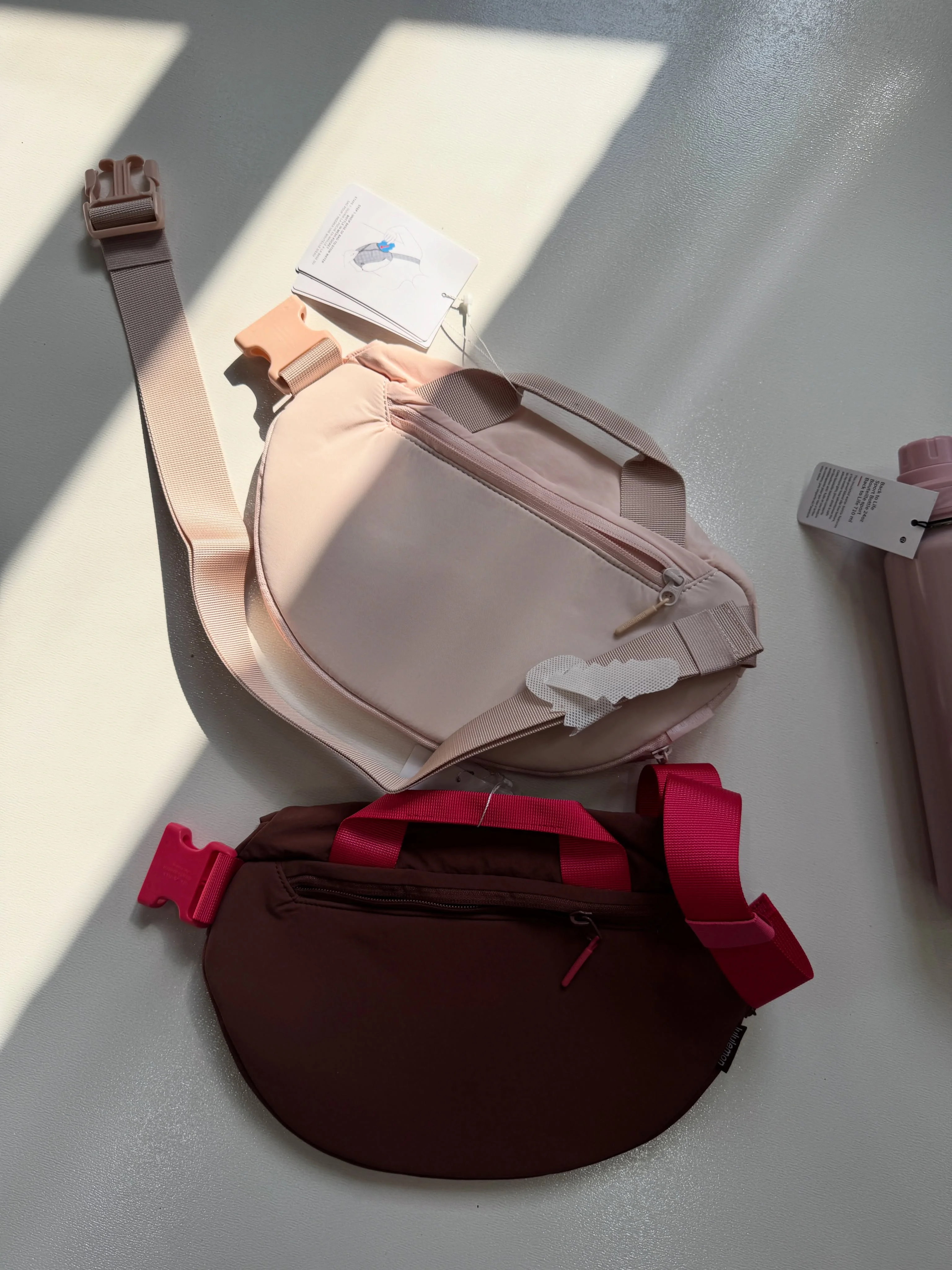 نمای پشت کراس بادی کرو Lululemon صورتی با بند پهن و تگ محصول؛ کیف قهوه‌ای در پایین