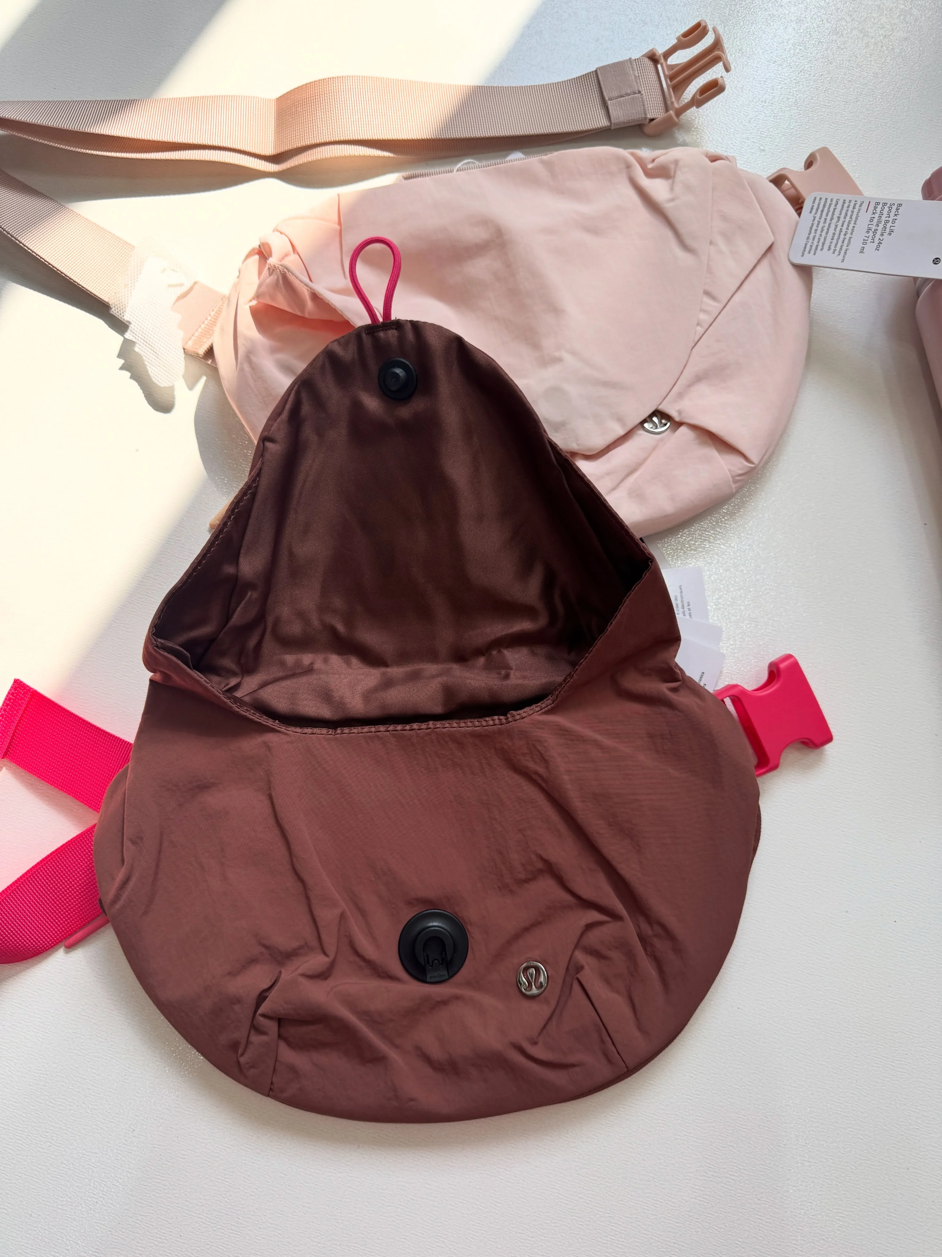 قفل‌های مگنتی و زیر درپوش باز کراس بادی کرو Lululemon قهوه‌ای؛ کیف صورتی در پس‌زمینه