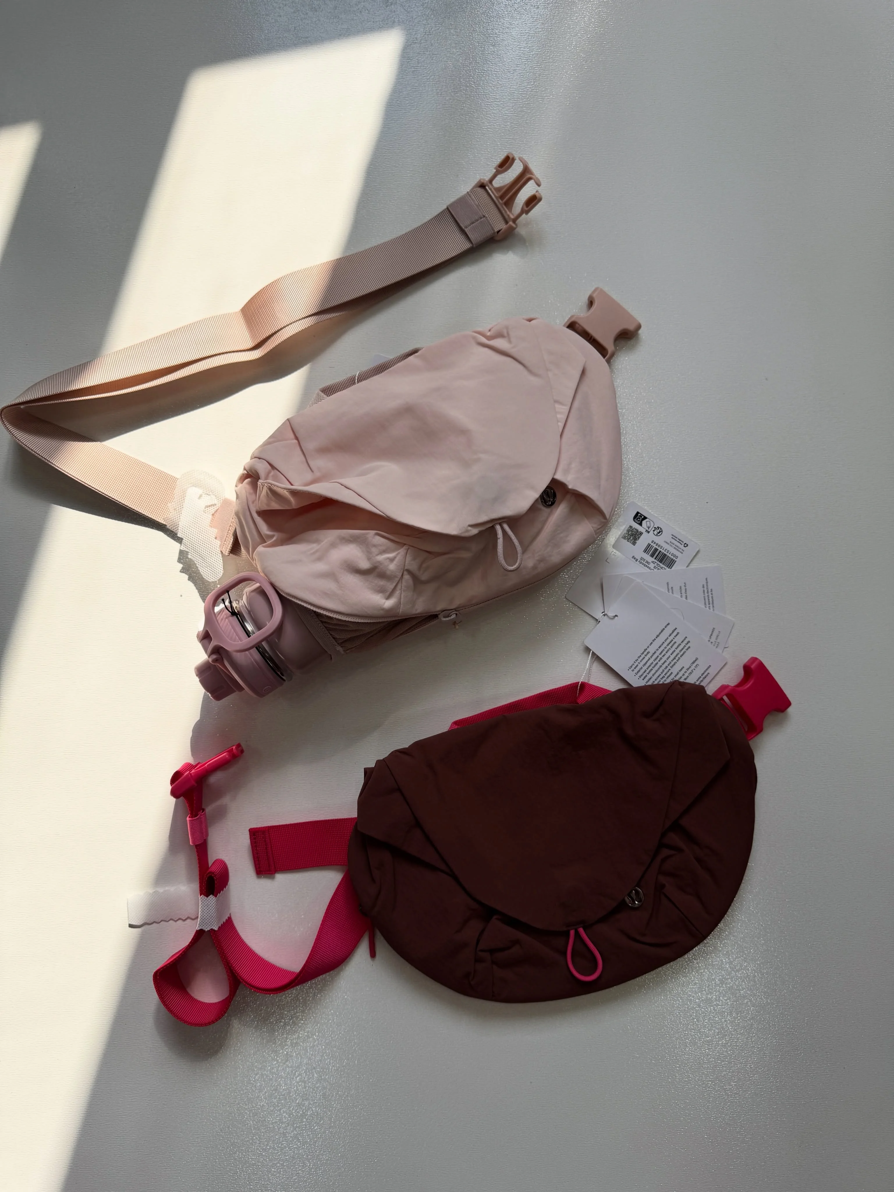 کراس بادی کرو Lululemon صورتی با بطری در نگهدارنده توری کنار کیف قهوه‌ای