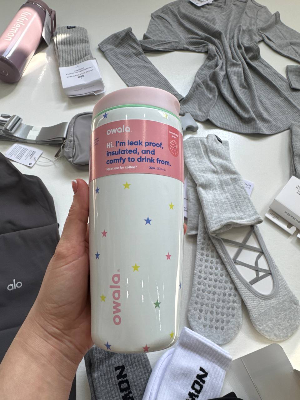 کافی کاپ Owala 20oz سفید با ستاره‌های رنگی، لوگوی صورتی و برچسب ظرفیت ۵۹۰ میلی‌لیتر در دست