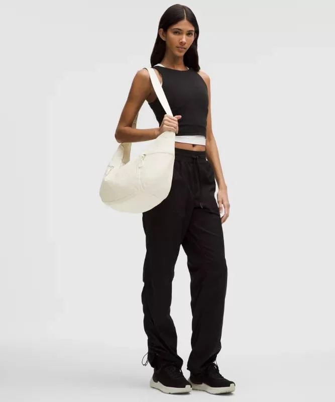 کیف اسلوچی اسلینگ Lululemon 13L شیری روی شانه مدل با لباس مشکی؛ نمایش فرم افتاده کیف