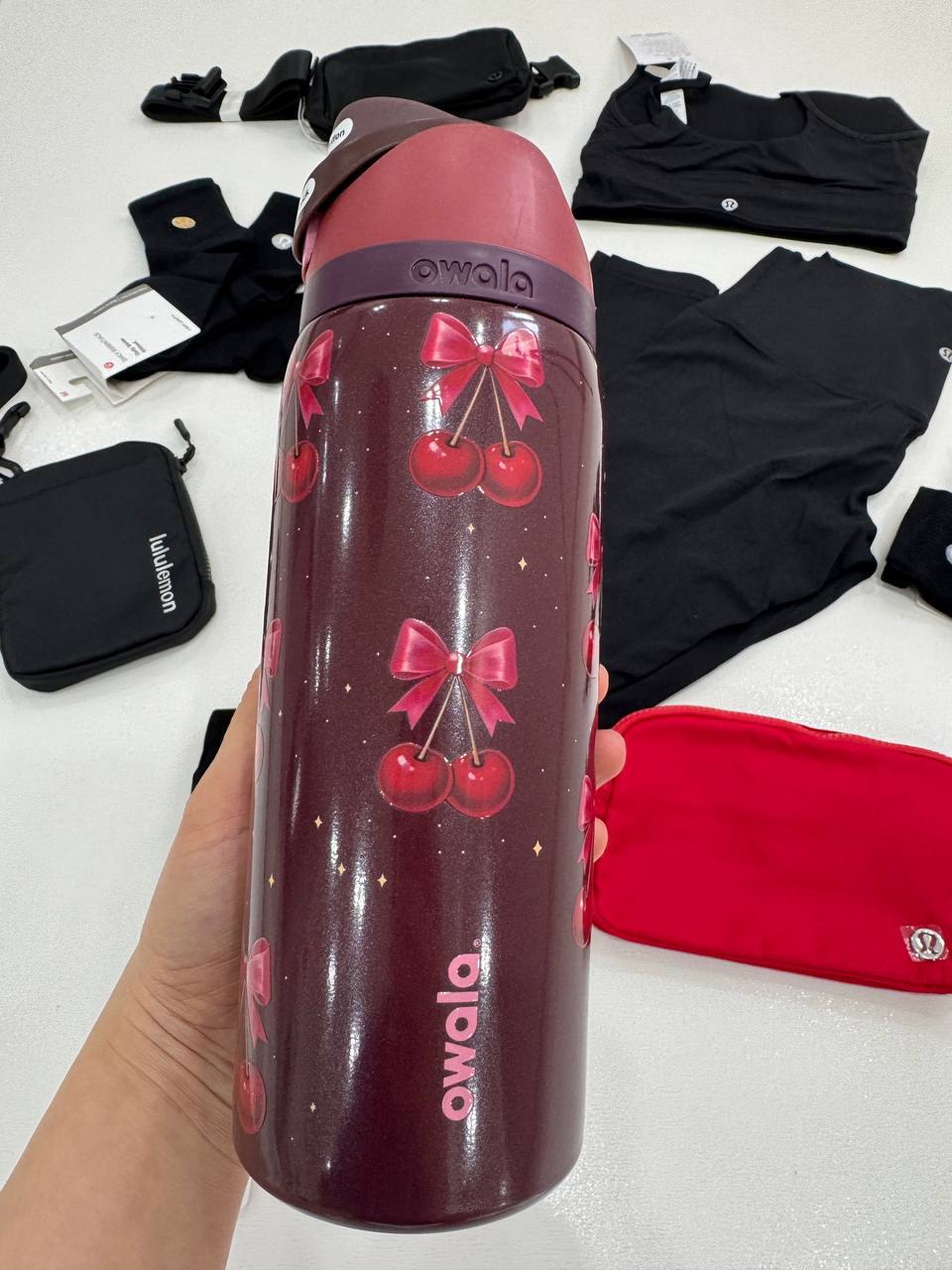 باتل Owala 32oz، باتل قرمز شفاف Owala 32oz با طرح گل‌های صورتی در دست