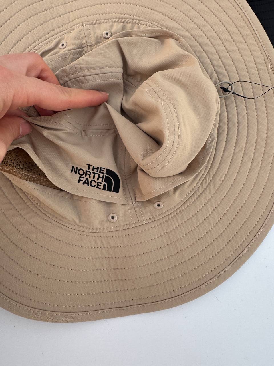 نمای نزدیک تاج کلاه باکت North Face کرم با لوگوی مشکی، سوراخ‌های تهویه و لبه دوخت‌دار