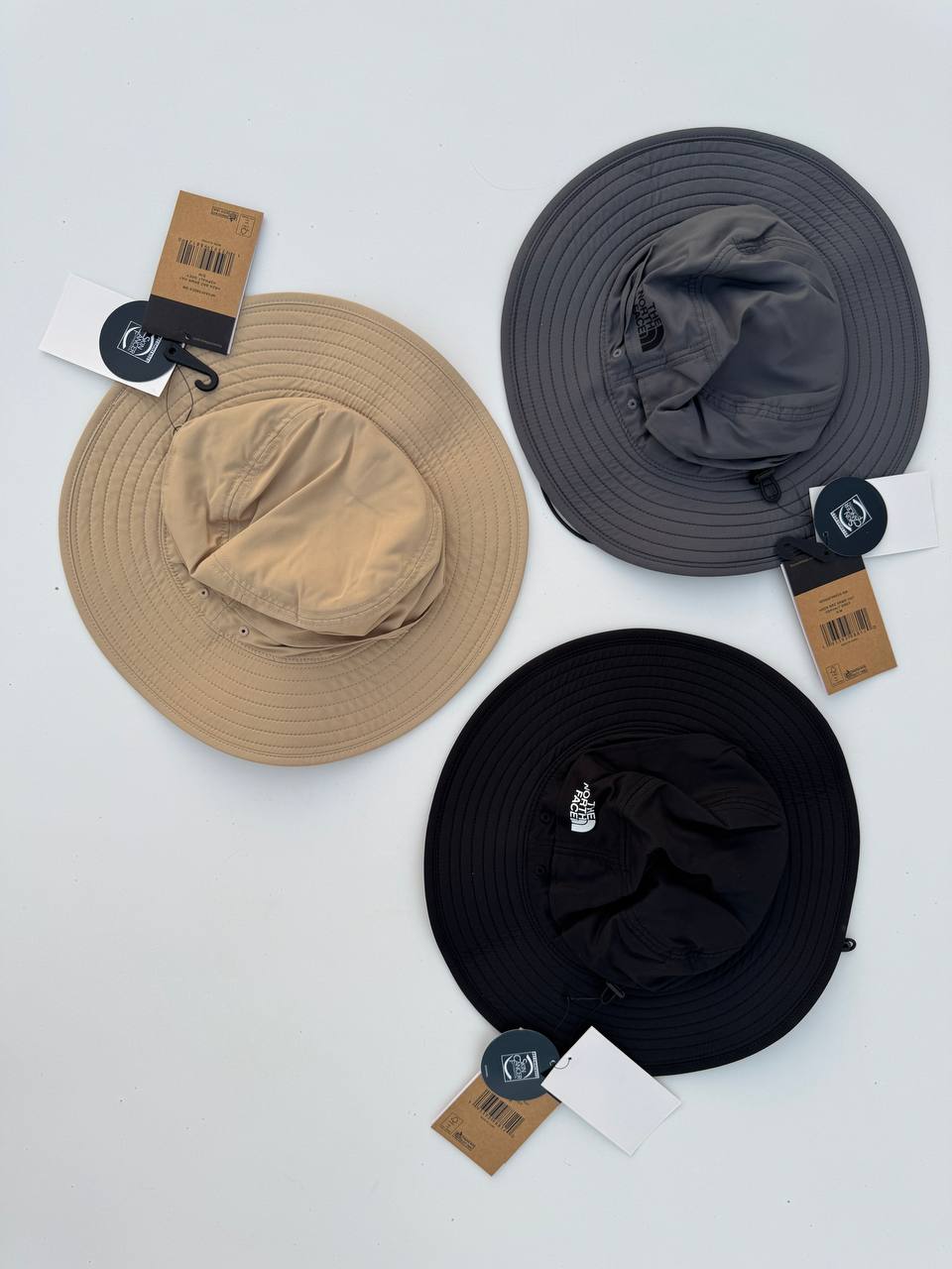 نمای بیرونی سه کلاه باکت North Face کرم، طوسی‌تیره و مشکی با تاج پارچه‌ای و لبه دوخت‌دار