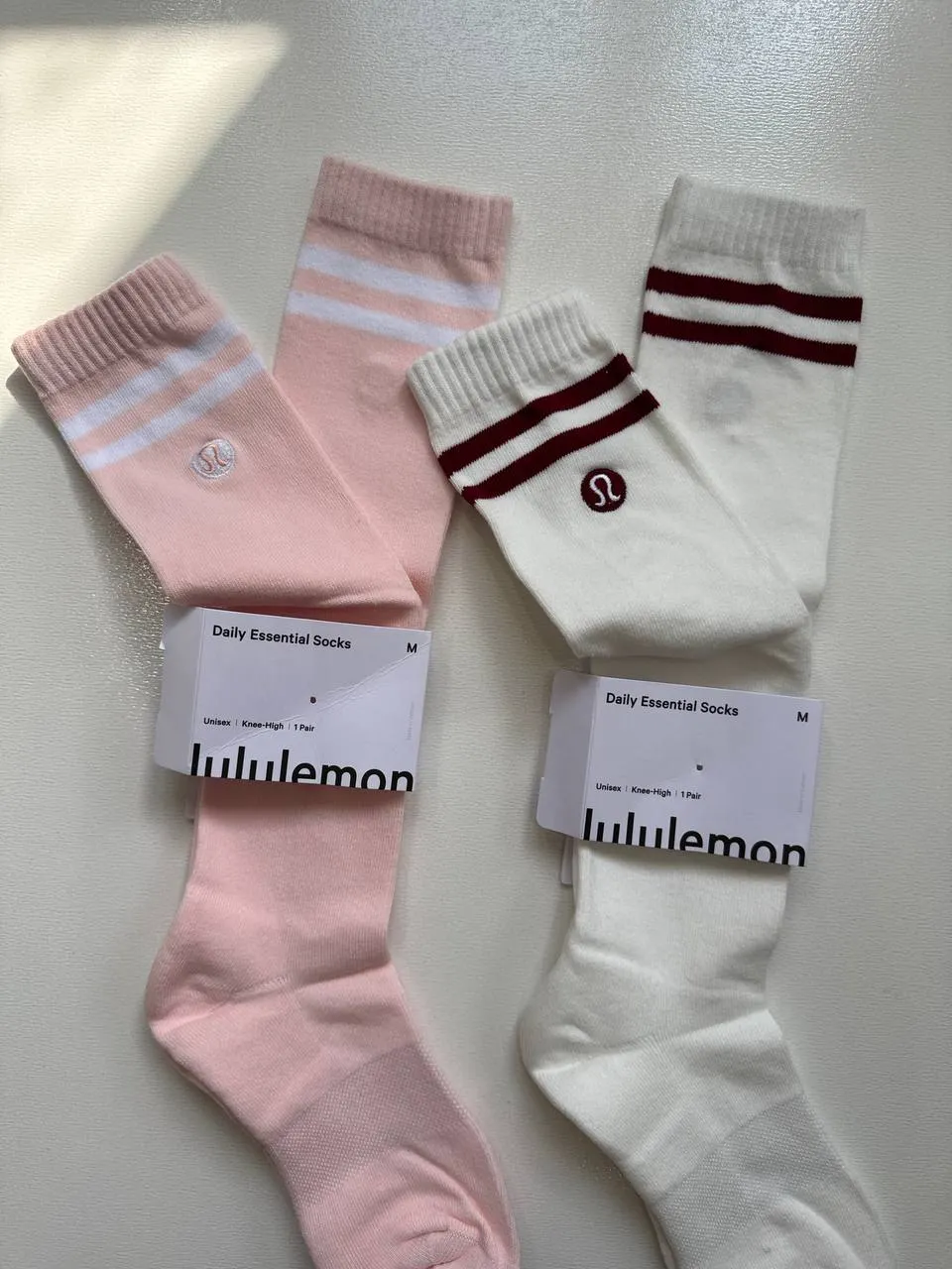 جزئیات بالای ساق جوراب Lululemon Knee-High در دو رنگ صورتی خط سفید و سفید خط زرشکی با لوگوی دوخت‌شده