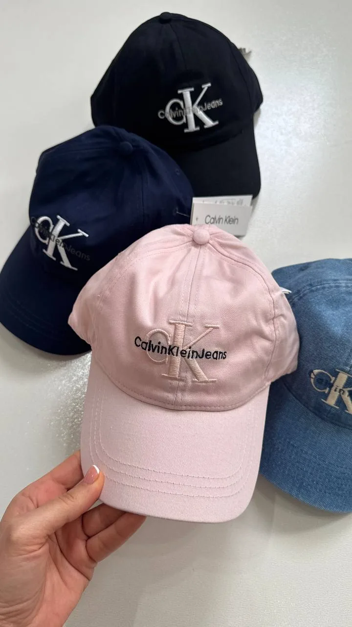 نمای نزدیک گلدوزی CK و نوشته Calvin Klein Jeans روی کلاه بال کپ صورتی، کنار سایر رنگ‌ها